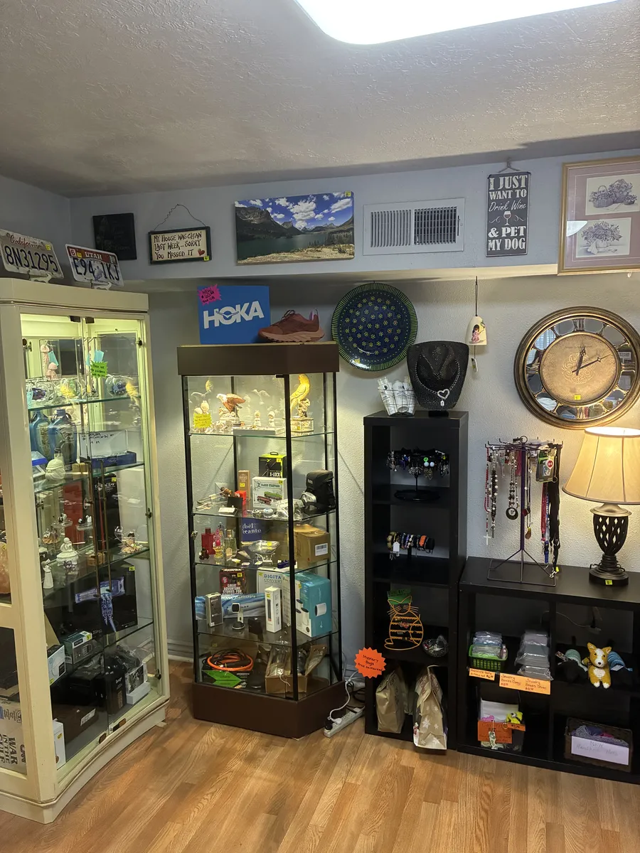 A glass cabinet, wall art, clocks and jewelry displays in a corner of BAM Thrift store