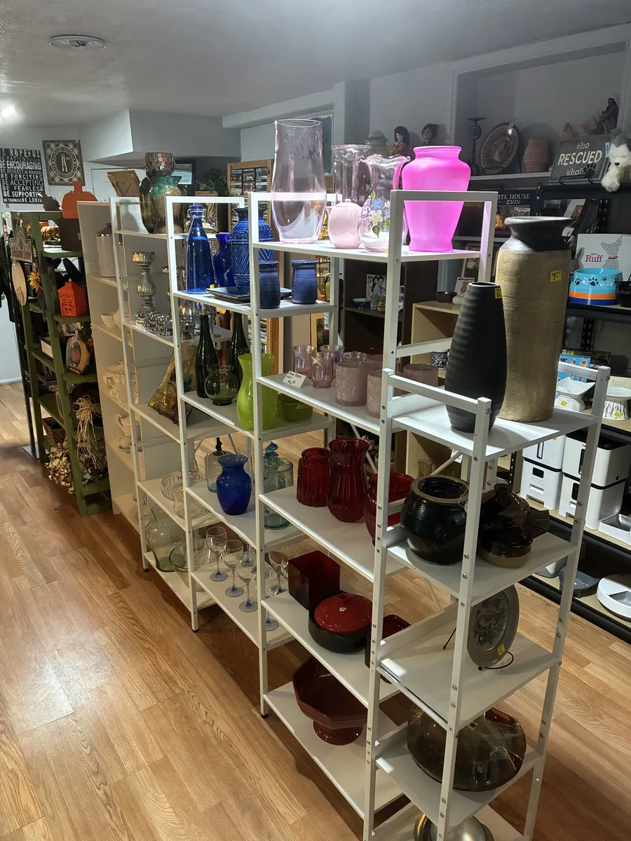Open shelves holding glass vases, colorful pitchers and decorative glassware at BAM Thrift store