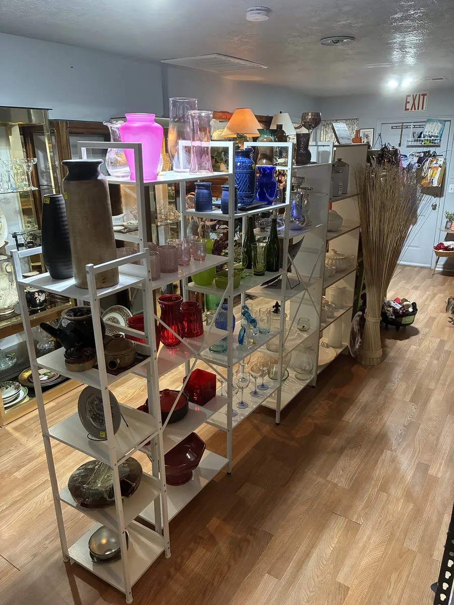 Shelves of colorful glassware and household decorations beside an aisle at BAM Thrift store