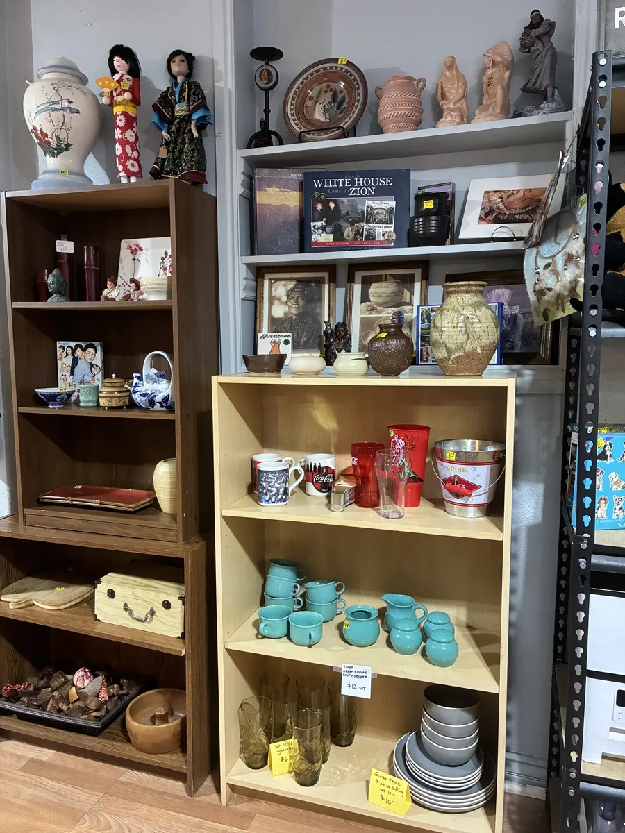 Wooden shelves displaying dishes, cups, vases and figurines at BAM Thrift store