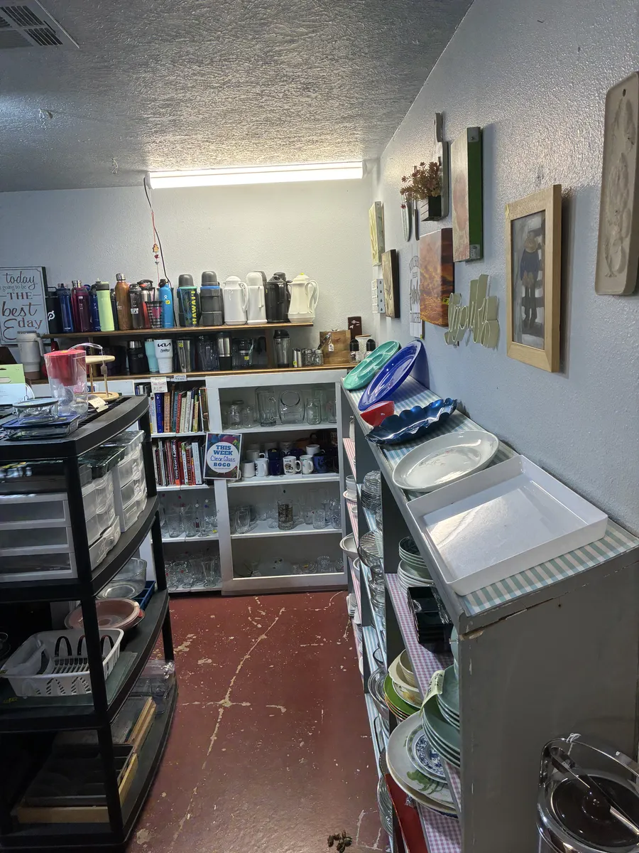 A narrow aisle of plates, trays, glasses and kitchen containers at BAM Thrift store