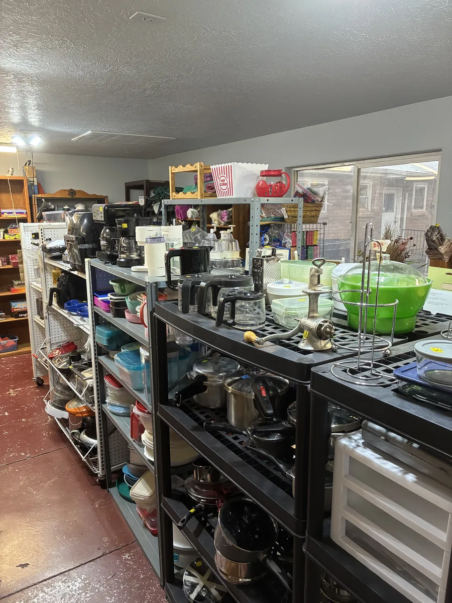 Coffee makers, kitchen tools and cookware displayed on shelves by a window at BAM Thrift store